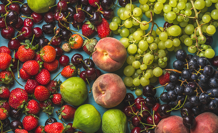 Uvas verdes, cereja, morango, pêssego e figo espalhados na mesa.