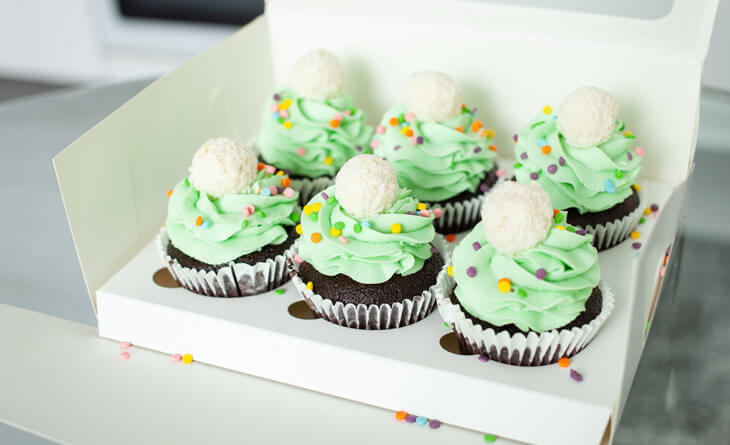 Caixa branca com seis cupcakes decorados em verde.
