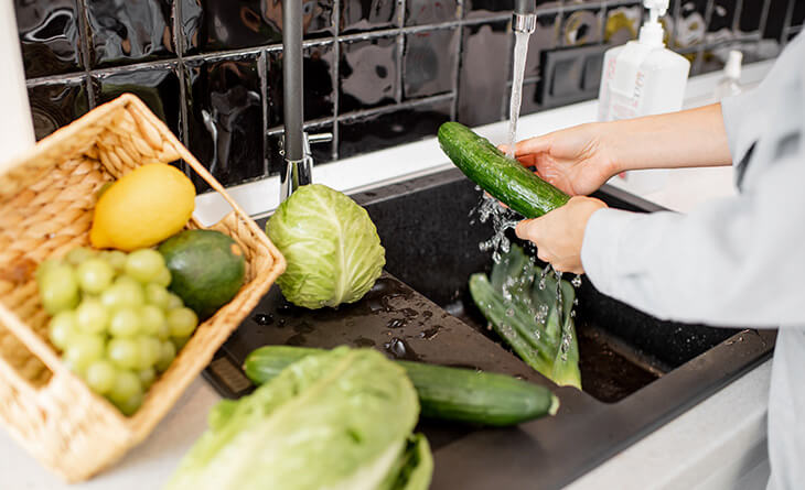 Mulher lavando as verduras na pia da cozinha.