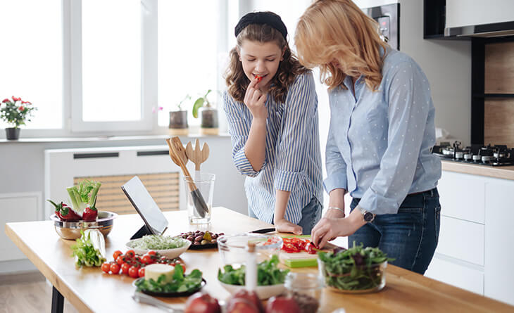 Mãe e filha de camisas azuis cozinhando o almoço de dia das mães juntas.