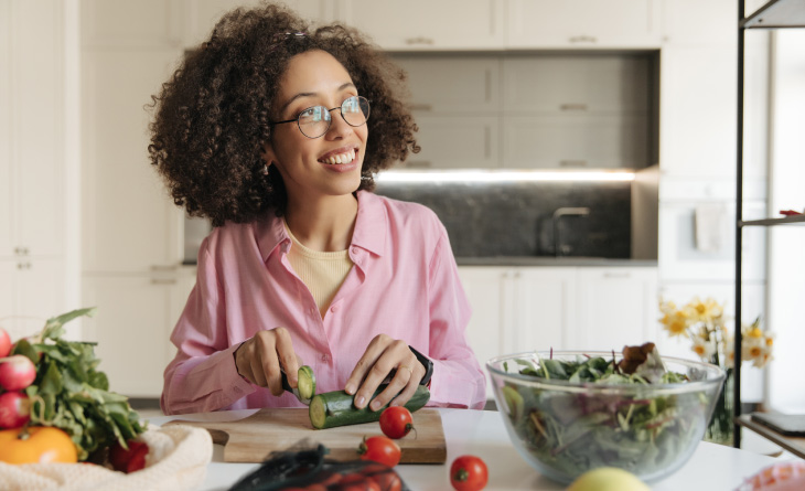 Mulher cortando um pepino para a salada que está em sua frente.