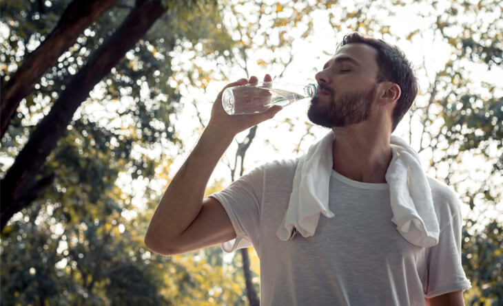 Homem bebendo água ao ar livre.