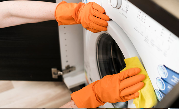 Mulher com luvas de borracha limpando a máquina de lavar.