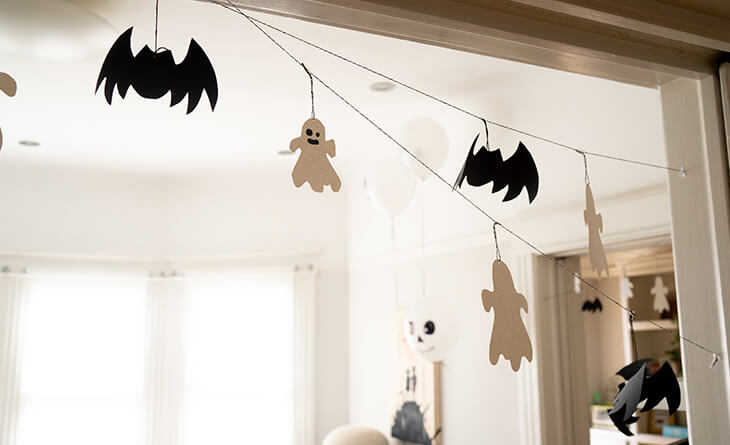 Morcegos e fantasmas de papel pendurados por um fio ao redor do batente da porta.
