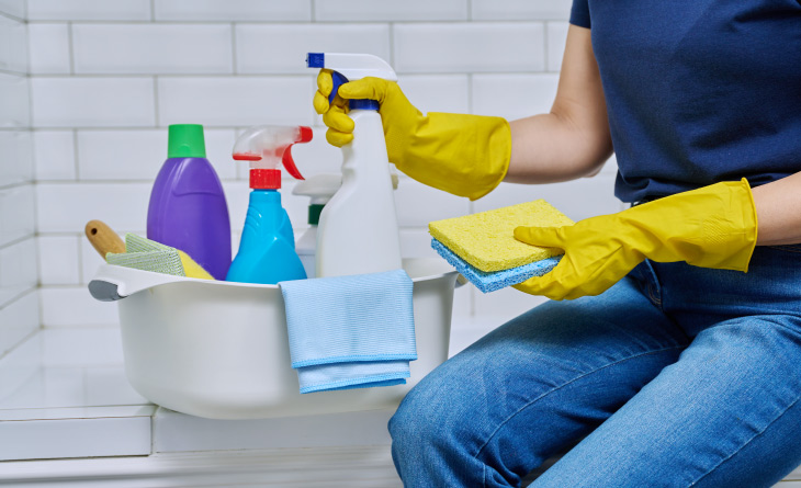 Mulher com luvas amarelas de borracha segurando um produto de borrifar.