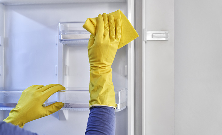 Mãos com luvas de borracha amarela limpando a geladeira.