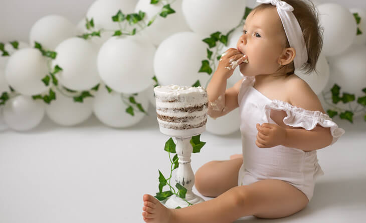 bebÃª de roupa branca comendo bolo de mesversario.