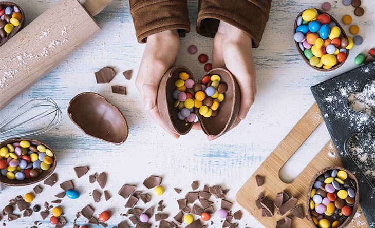 Criança partindo um ovo de chocolate recheado com bolinhas coloridas.