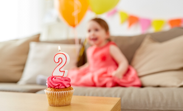 Cupcake de aniversário com vela de 2 anos com a bebê atrás.