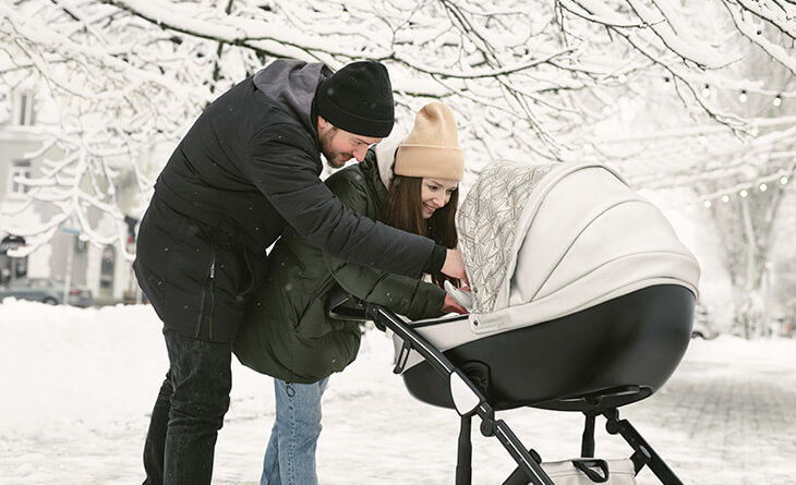 Casal com roupas de inverno fazendo carinho no bebê dentro do carrinho.