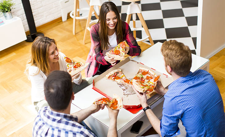 Dois homens e duas mulheres comendo uma pizza com pepperoni.