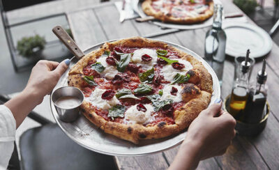 Pessoa levando uma pizza napolitana para a mesa.