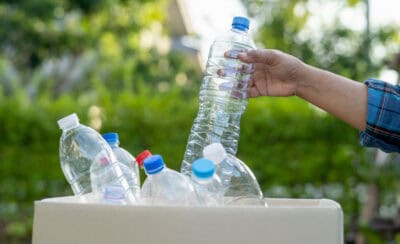Mão depositando garrafa PET em caixa.