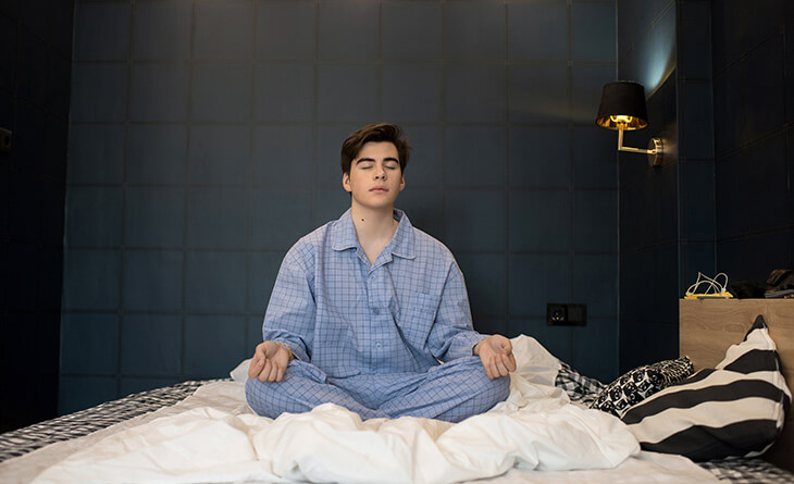 Homem de pijama azul mediando na cama antes de dormir. 