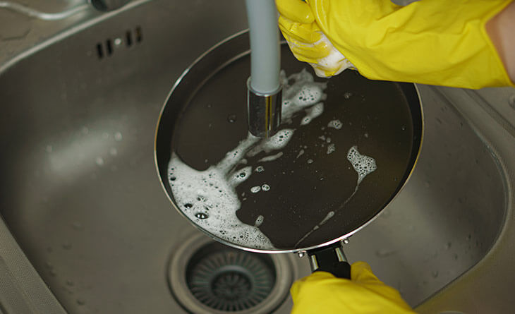 Mãos com luvas amarelas lavando a panela antiaderente.