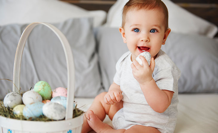 Bebê segurando ovo de páscoa próximo da boca.
