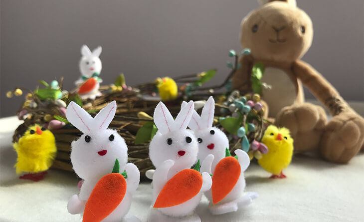 Três mini coelhos decorativos em frente a um ninho de vime.
