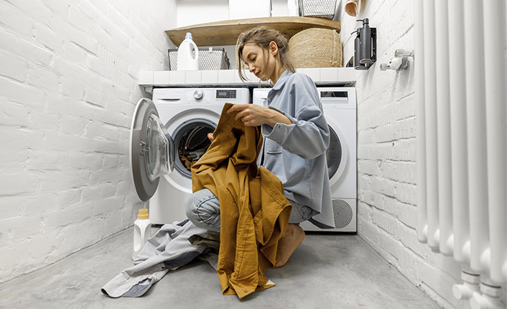 Mulher colocando as roupas na maquina de lavar.