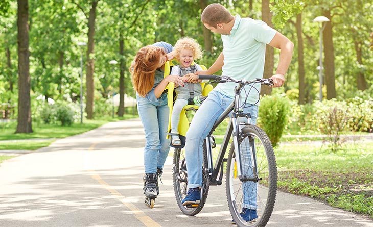 Pai e filha na bicicleta e mãe acompanhando na sequência.