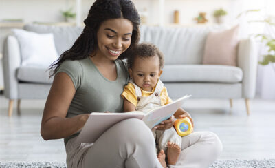 Mãe lendo livro para o bebê em seu colo.