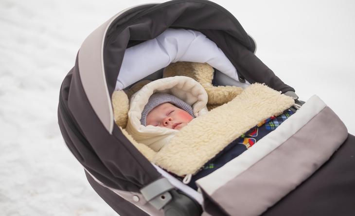Bebê com roupa de inverno dormindo no carrinho.