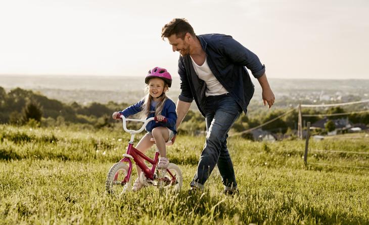 Pai ensinando a filha a andar de bicicleta.