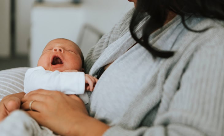 Bebê bocejando no colo da mãe.