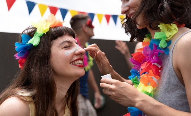 Mulher passando glitter no rosto de outra durante comemoração de carnaval.