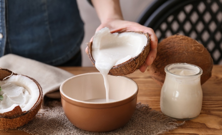 Mulher colocando o leite de coco direto da casca num bowl.