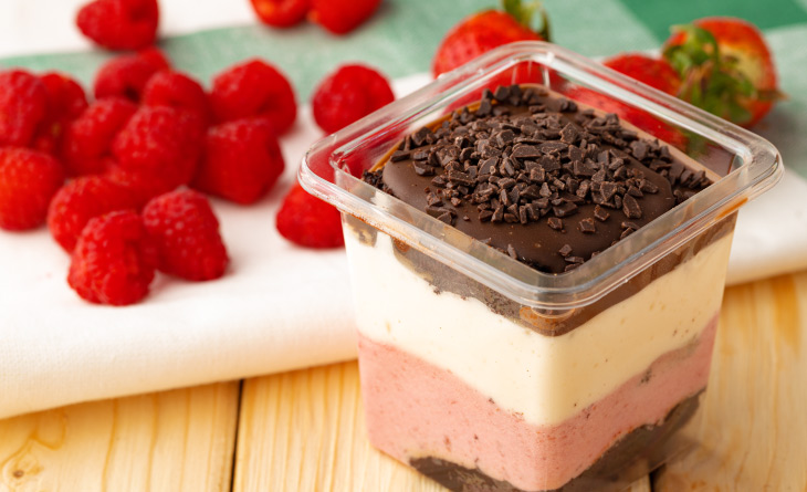 Bombom de morango num pote transparente ao lado de framboesas.