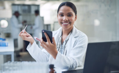 Mulher sorrindo e segurando um batom nude na mão.