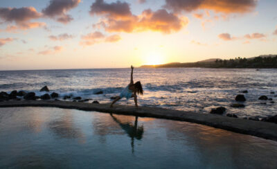 Mulher praticando yoga na praia.