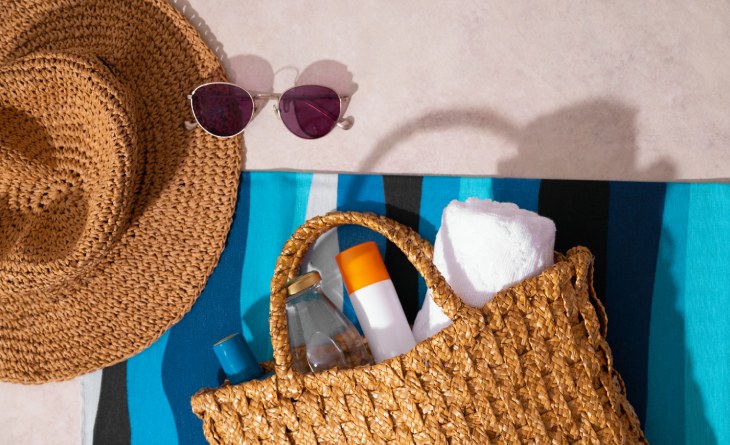 Bolsa de praia, com protetor e água, óculos de sol e chapéu de praia.