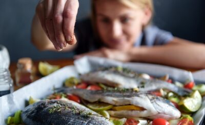Mulher colocando tempero no peixe.