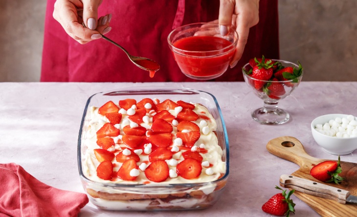 Mulher montando sobremesa com morango em travessa.