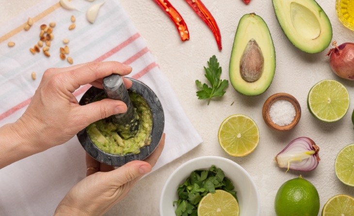 Mãos usando utensilio para amassar abacate num pote. 