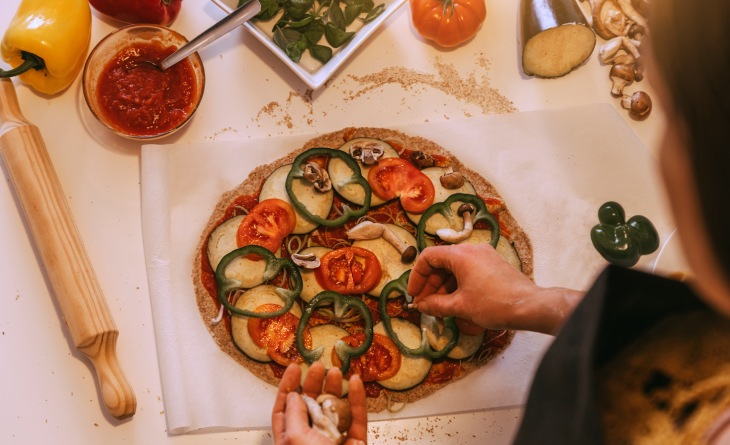 Pessoa montando pizza com legumes.