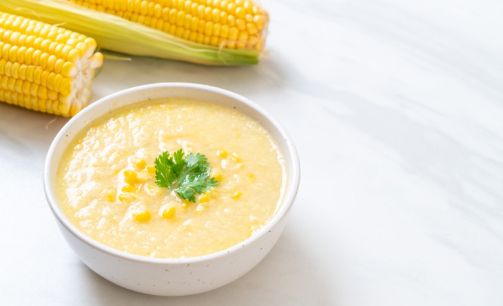 Pote com creme de milho ao lado de duas espigas.