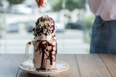 Caneca com milk-shake e bola de sorvete com calda e confeito no topo.