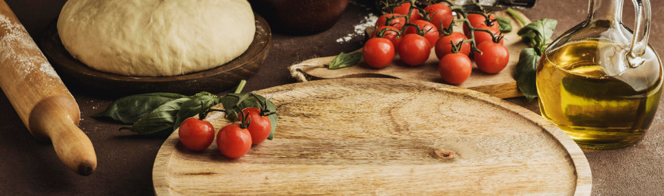 Tábua de madeira com tomate e massa de pizza.