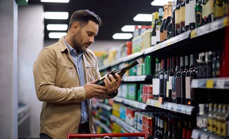 Homem escolhendo vinho no mercado.