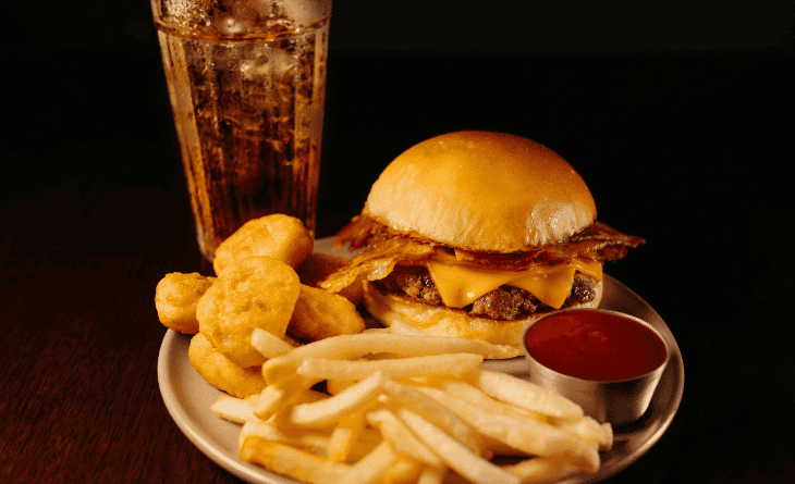 Prato com lanche, nugget e batata frita ao lado de copo de refrigerante.