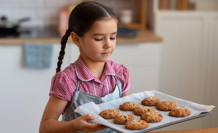 Menina segurando fornada de biscoitos.