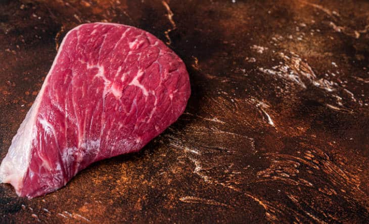 Pedaço de carne sobre tábua de madeira.
