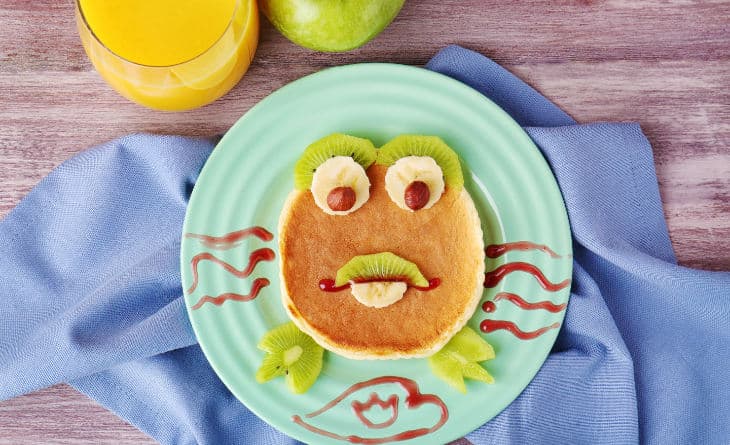 Panqueca com frutas e geleia formando figura divertida.