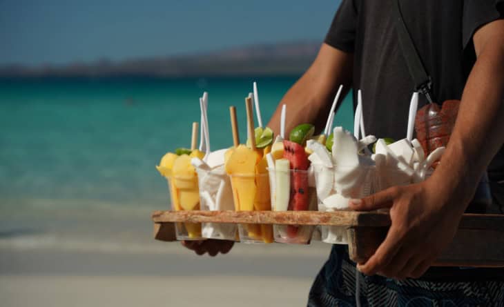 Homem carregando bandeja com frutas cortadas em copos plásticos.